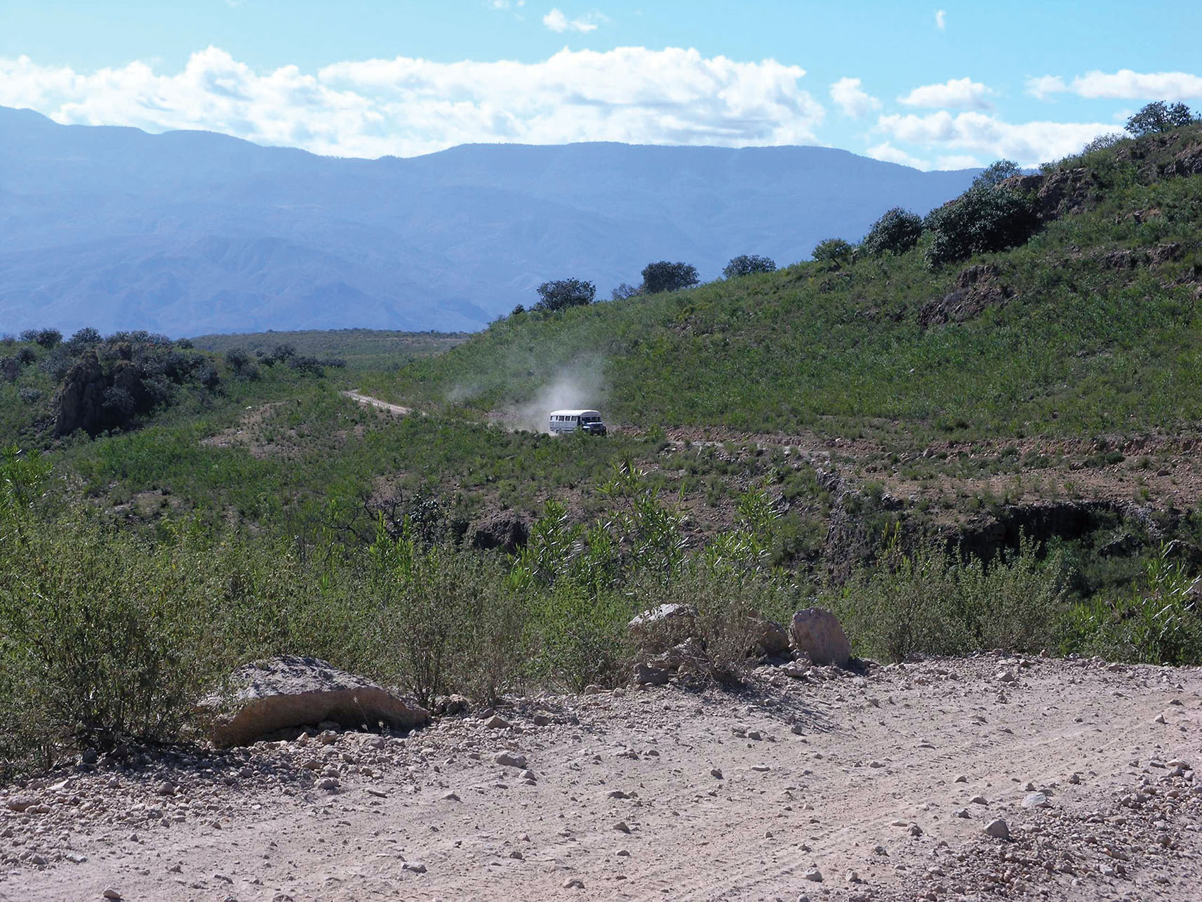 A lone bus kicks up a cloud of dust on a remote dirt road in the Mexican countryside. (Photo by Lon&Queta.)