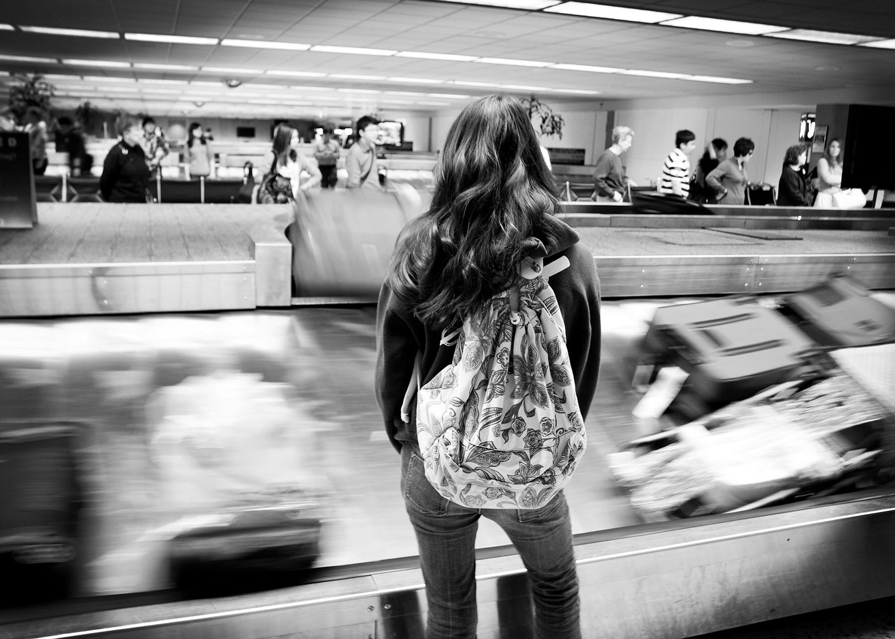 A young woman waits at the baggage claim carousel in an airport. (Photo by Tejas Califas.)