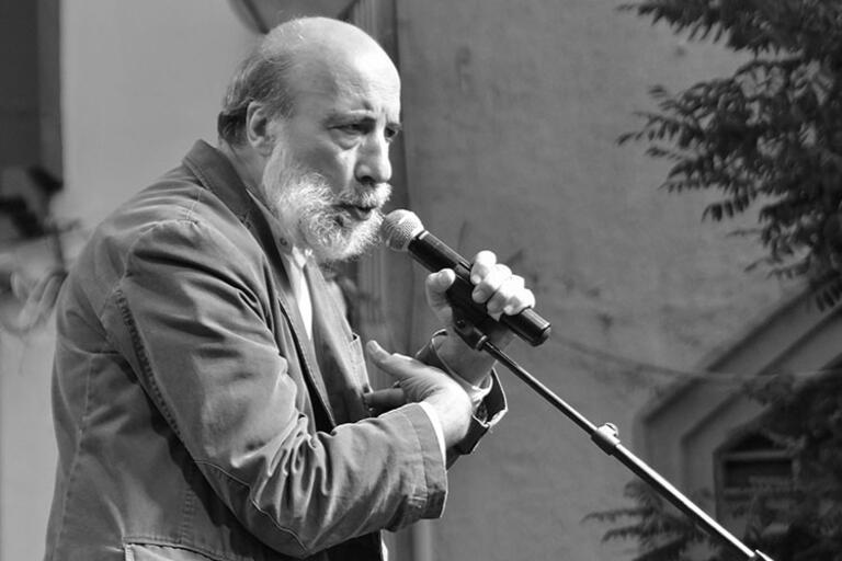 Raúl Zurita holding a microphone with one hand and the other hand over his heart