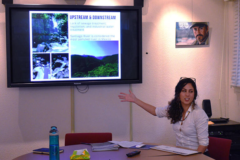 Francesca Rubino wearing a white blouse seating talking to the audience and pointing toward her slides
