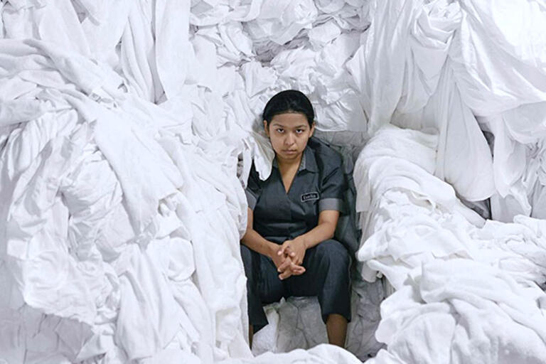 Image from "La Camarista." (Photo courtesy of Kino Lorber.) Woman seating surrounded by white bed sheets