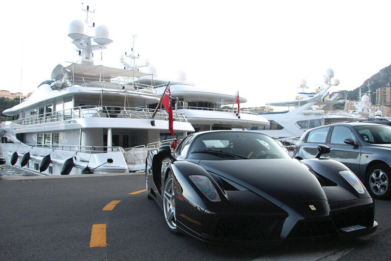 Lifestyles of the “transnational global plutocratic overclass”: a Ferrari parked in front of a row of yachts, Monaco. (Photo by Damian Morys Photography.)