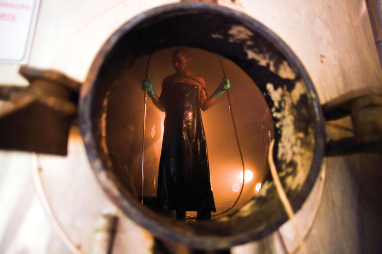 Brazilian workers in rubber aprons with steam hoses clean vaporizing tanks in a São Francisco ethanol and sugar plant. (Photo by Ricardo Funari.)