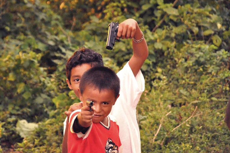 Nicaraguan kids point guns at each other and the camera while playing cops and robbers. (Photo by Eric Molina.)