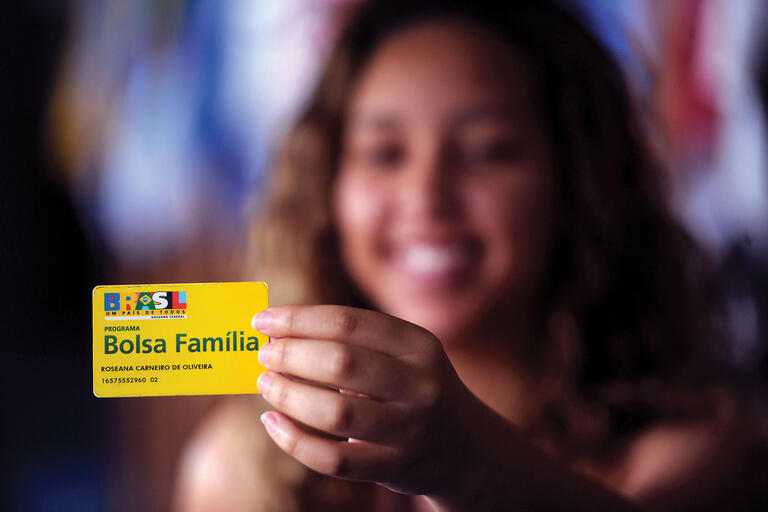A woman holds up a Brazilian Bolsa Familia identification card in 2014. (Photo courtesy of Senado Federal do Brasil.)