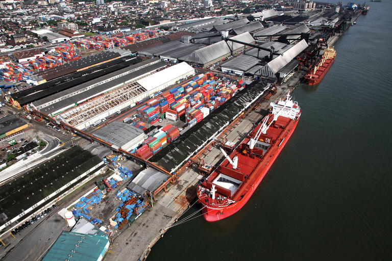 The port of Santos, Brazil. (Photo courtesy of the Program for Accelerated Growth PAC.) The busy port of Santos, Brazil, with ships being loaded by overhead cranes from a large storage facility for shipping containers.. (Photo courtesy of the Program for Accelerated Growth PAC.)