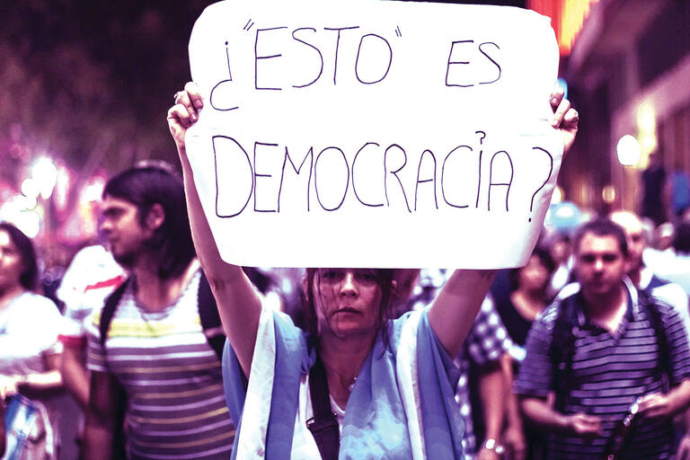 A woman holds a sign saying “‘This’ is democracy?” during a protest in Argentina. (Photo by Martín Iglesias.)