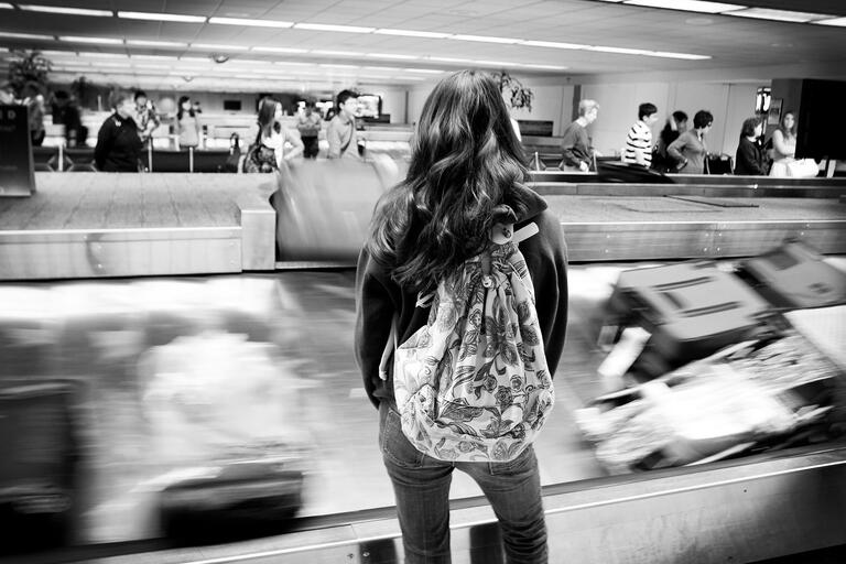 A young woman waits at the baggage claim carousel in an airport. (Photo by Tejas Califas.)