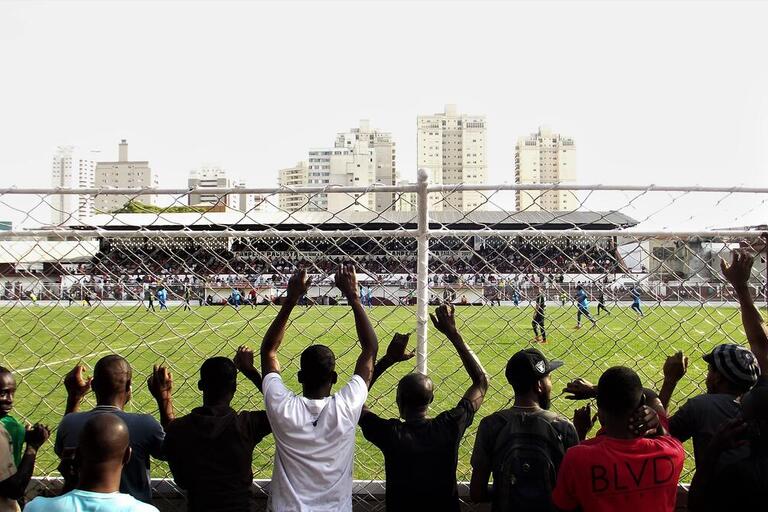 Haitians watch a soccer game in Brazil. (Photo by João Vitor Campos.) Men line up against a fence to watch a soccer game