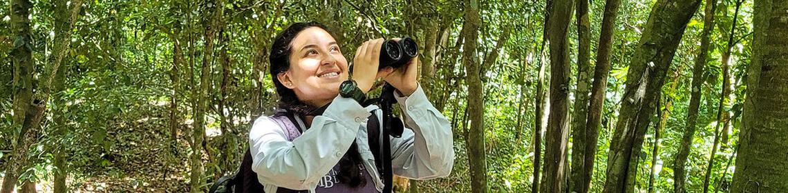 2022 CLAS Field Research Grant recipient Anais Cardenas Navarette literally in the field, observing in a woodland with binocular