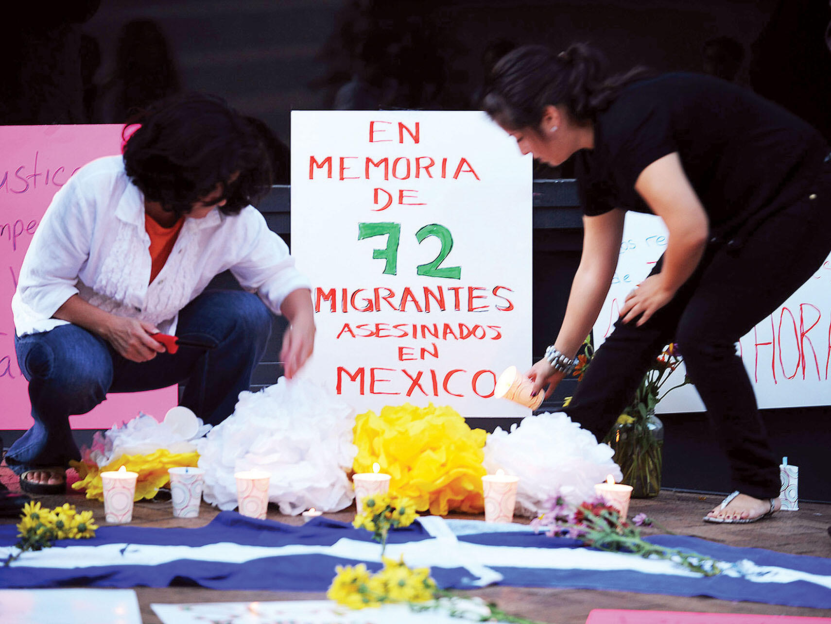 Women stoop to light candles at a street altar for the 72 murdered migrants. (Photo by Lenin Nolly Araujo.)