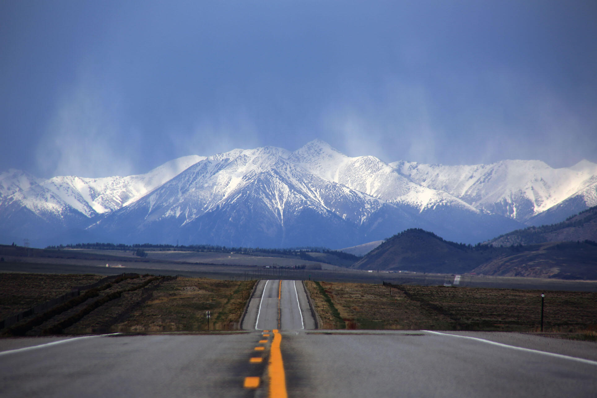 A road vanishes into the distances towards snow-capped mountains in a Colorado landscape. (Photo by Jason Leverton.)
