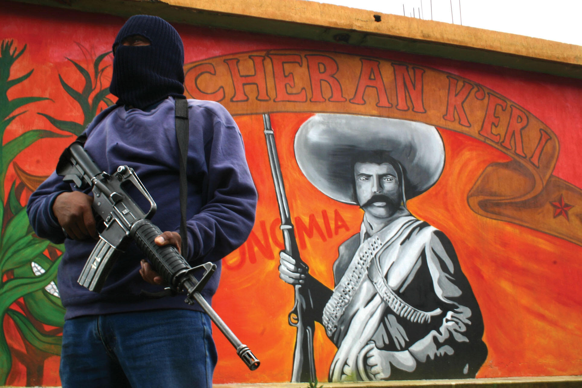 A community guard member with an assault rifle in front of a mural of Zapata. (Photo by Juan José Estrada Serafín.)