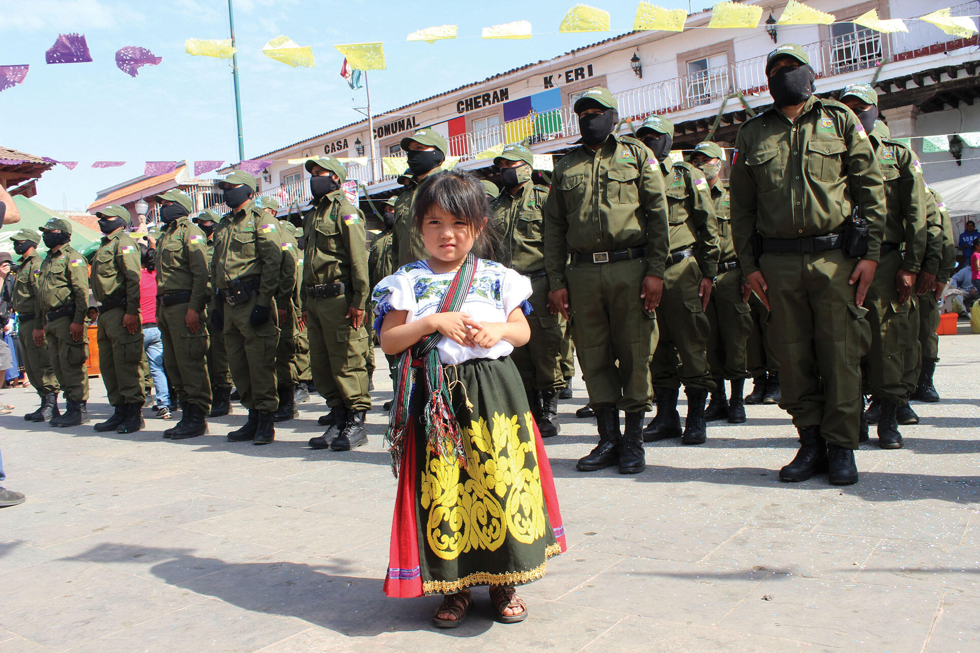 A young girl in a festival dress stands before an assembly of Cherán’s community guard. (Photo by Juan José Estrada Serafín.)