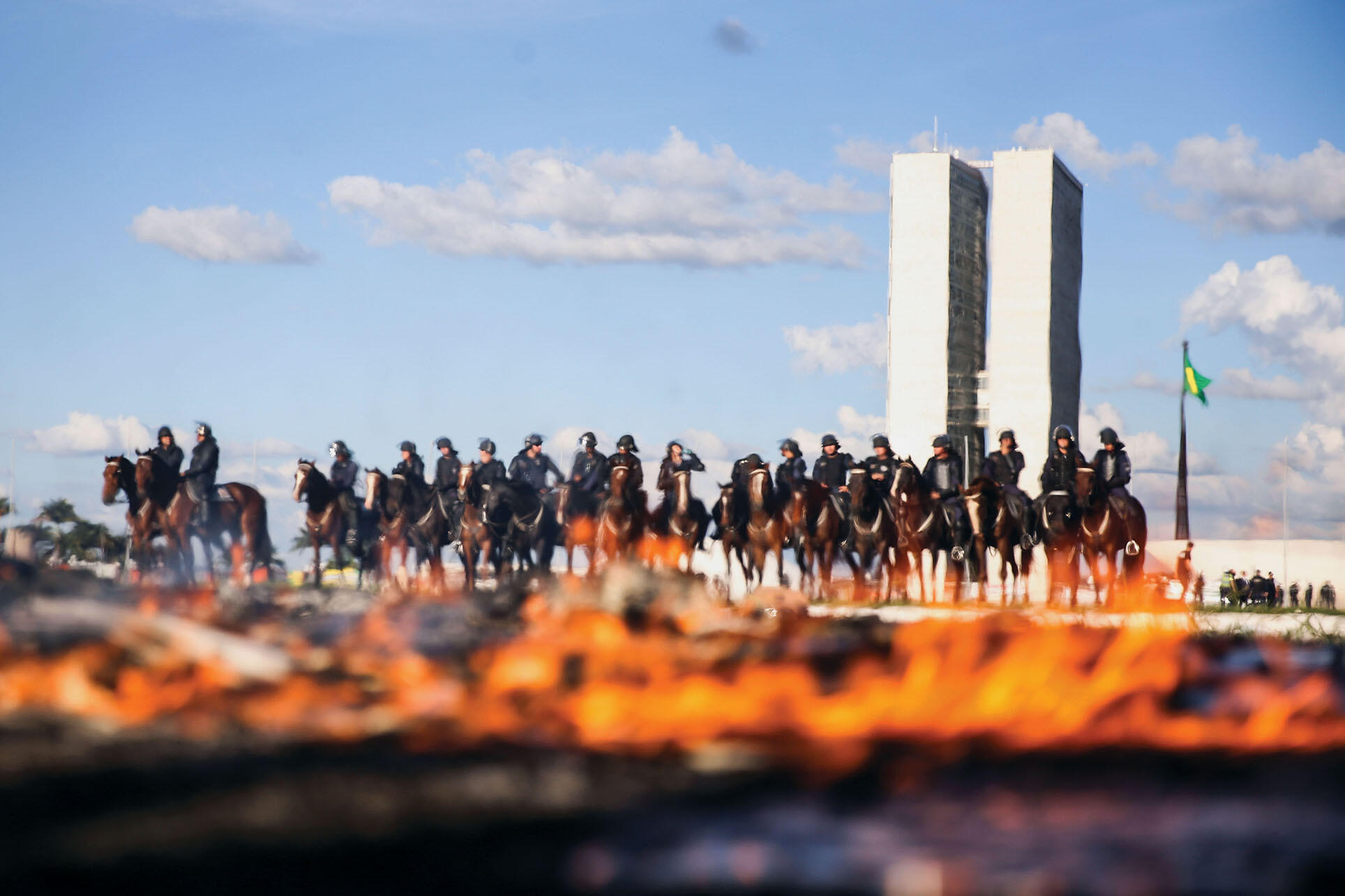 Mounted police shown through the flames of a fire lit at an anti-government demonstration during votes overturning progressive policies on worker rights and pensions, May 2017. (Photo by Marcelo Camargo/Agência Brasil Fotografias.)