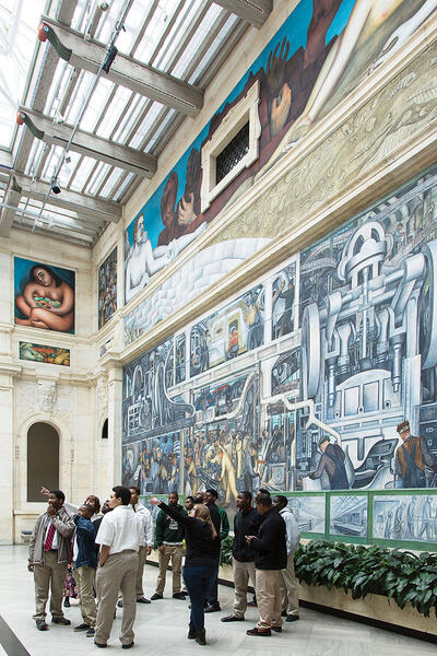 A docent points out parts of “Detroit Industry” to students visiting the DIA. (Photo © 2017 Detroit Institute of Arts.)